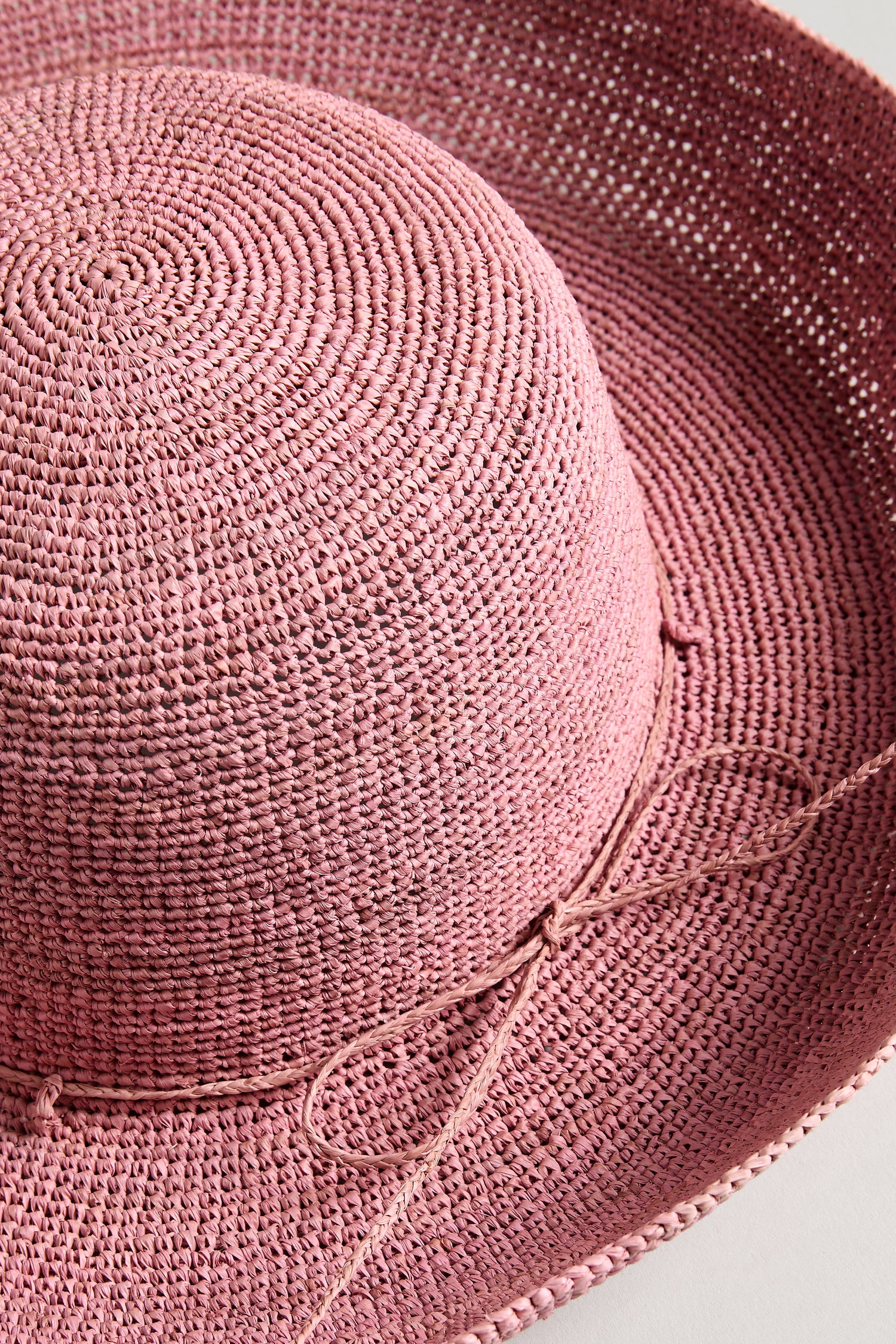 A close-up of the Handwoven Wide Brim Raffia Hat, crafted in pink raffia from Madagascar, showcasing a wide brim and a thin decorative string tied at the crown.
