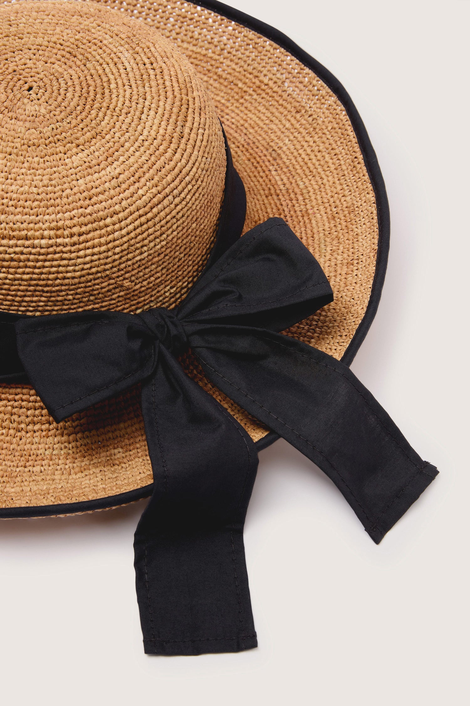 Hand-crafted Ribbon Raffia Hat with black ribbon detail on white background.