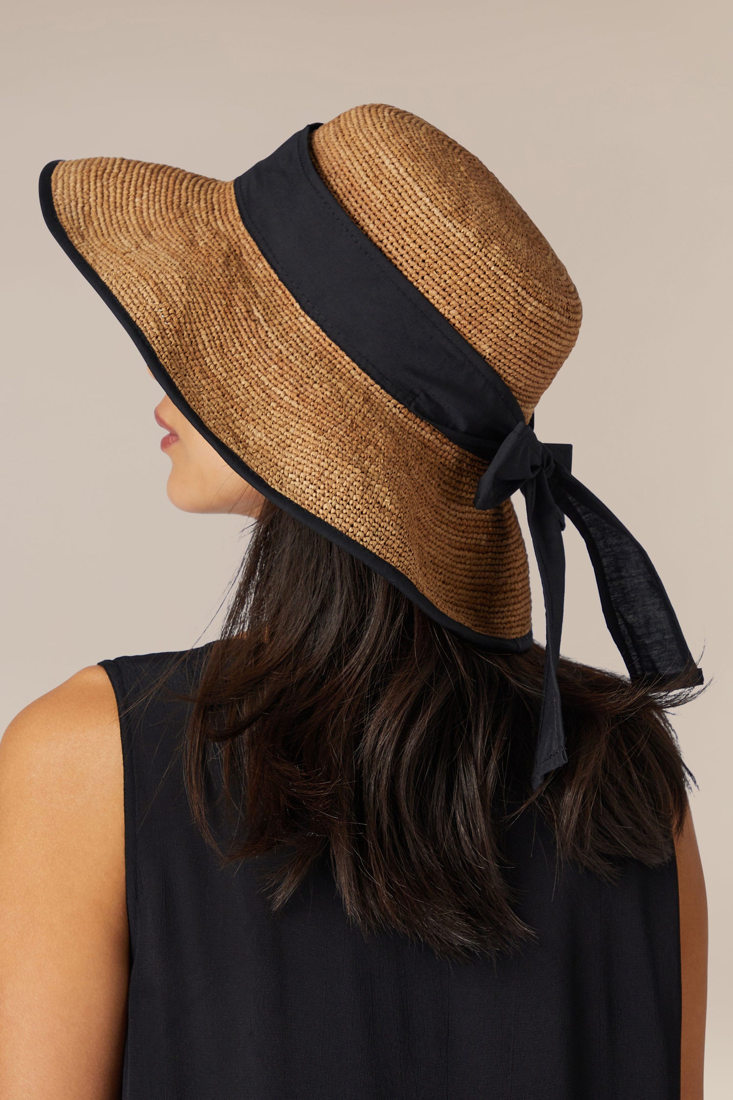 A woman in a black dress wearing a Hand-crafted Madagascar Ribbon Raffia Hat.