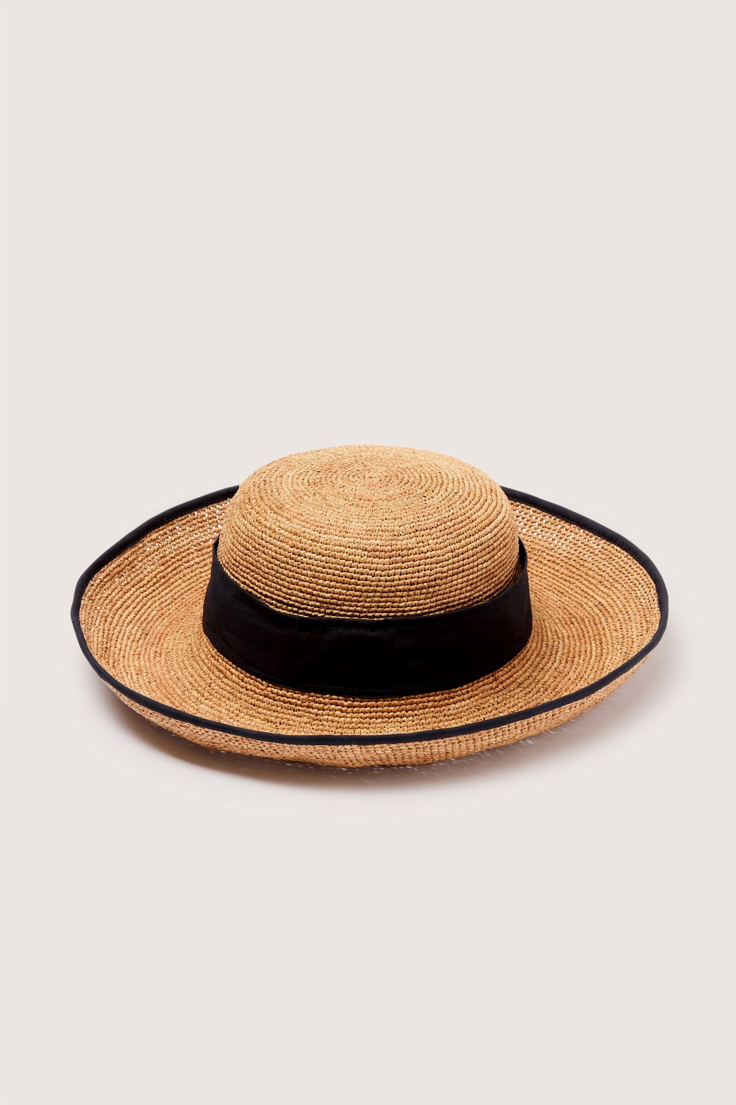 A hand-crafted Ribbon Raffia Hat with a black ribbon isolated on a neutral background.