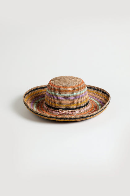 The Handwoven Raffia Rainbow Stripe Hat from Madagascar features a wide brim and multicolored horizontal stripes, displayed against a plain white background.