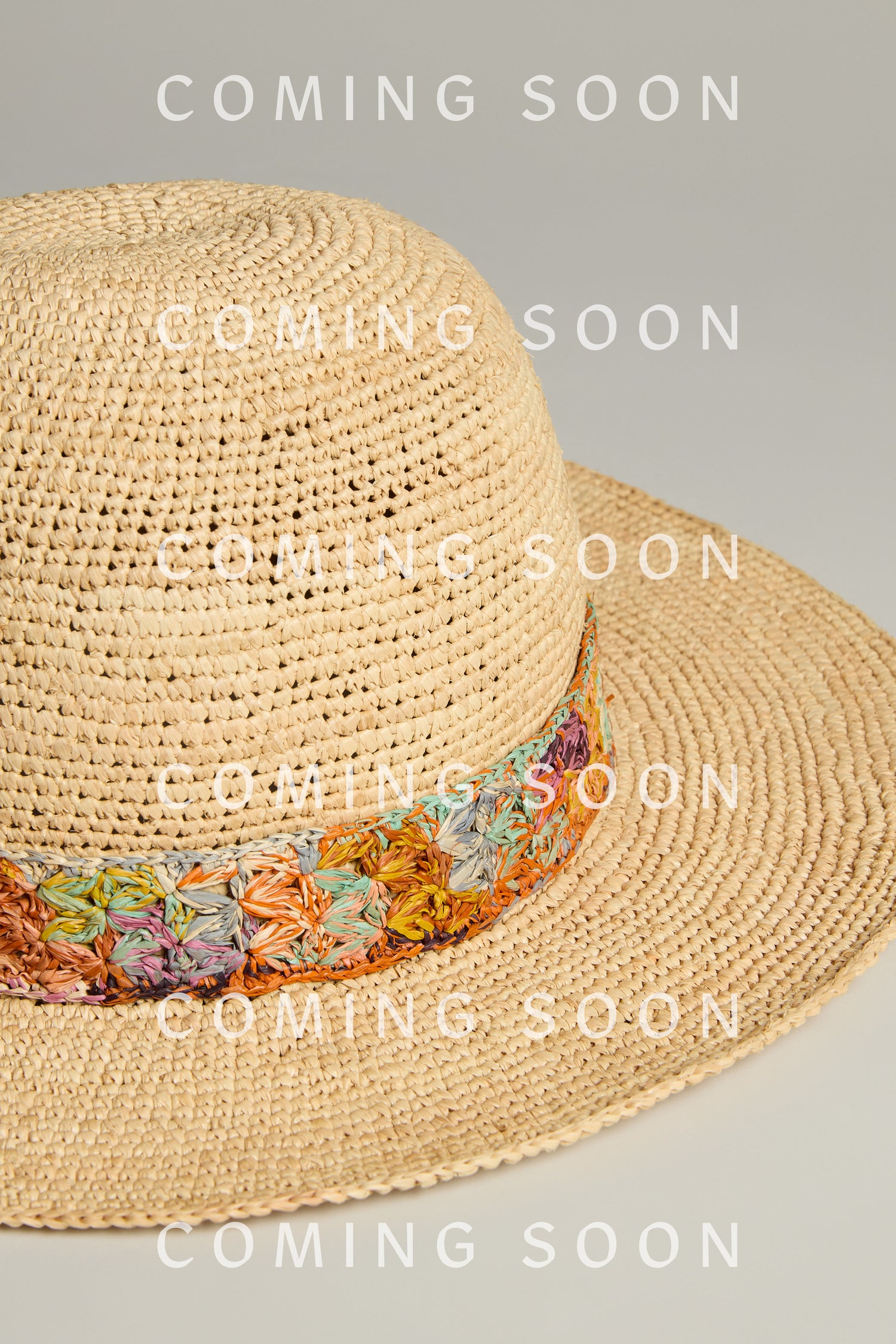 A Handwoven Flore Raffia Hat is set against a plain background with a colorful floral band. The words "COMING SOON" and the mysterious code RABB7KAL are scattered across the image, adding intrigue to this stylish reveal.