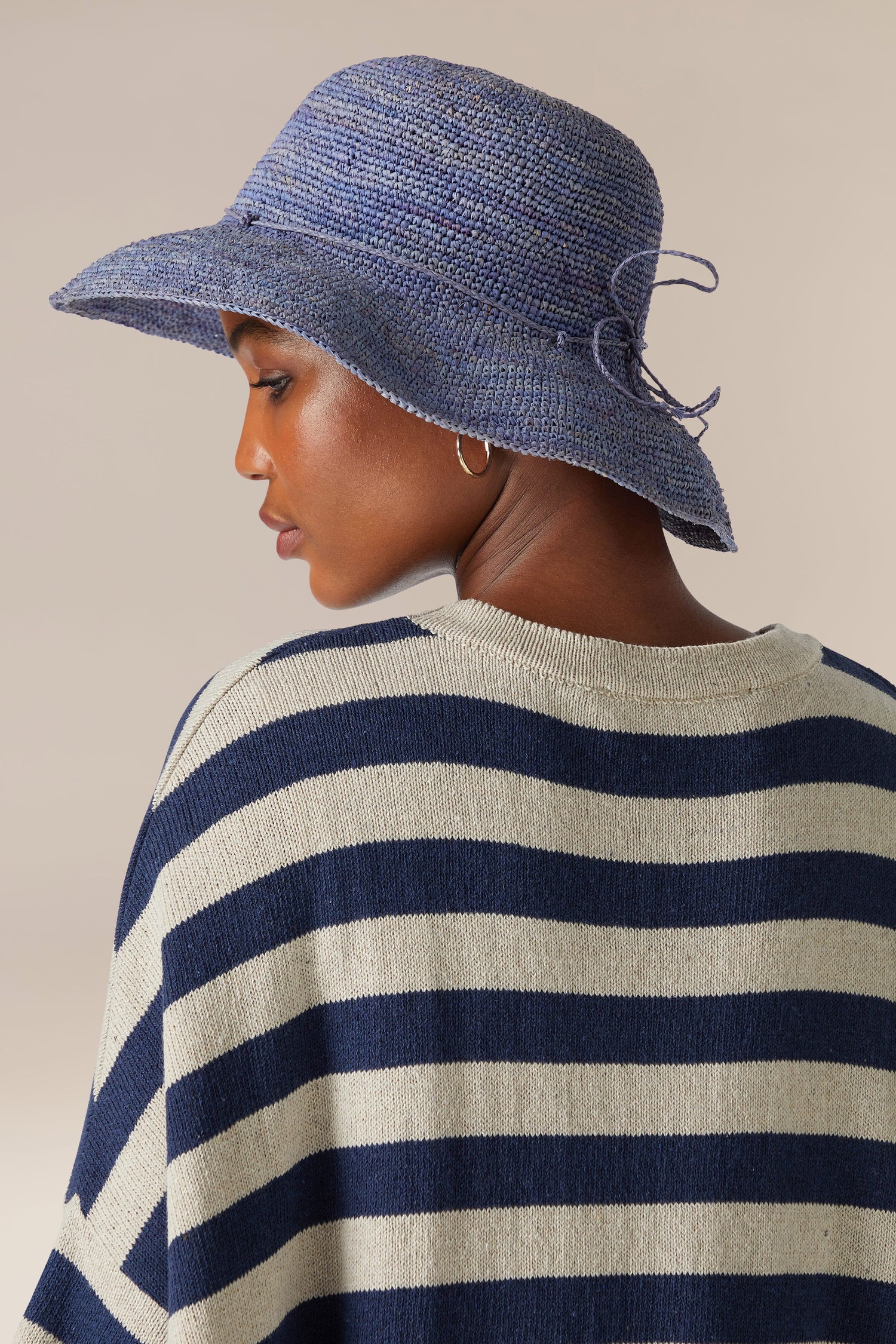 A woman in a striped sweater and a hand-crafted Raffia Hat, viewed from behind with a focus on the hat and her neckline.