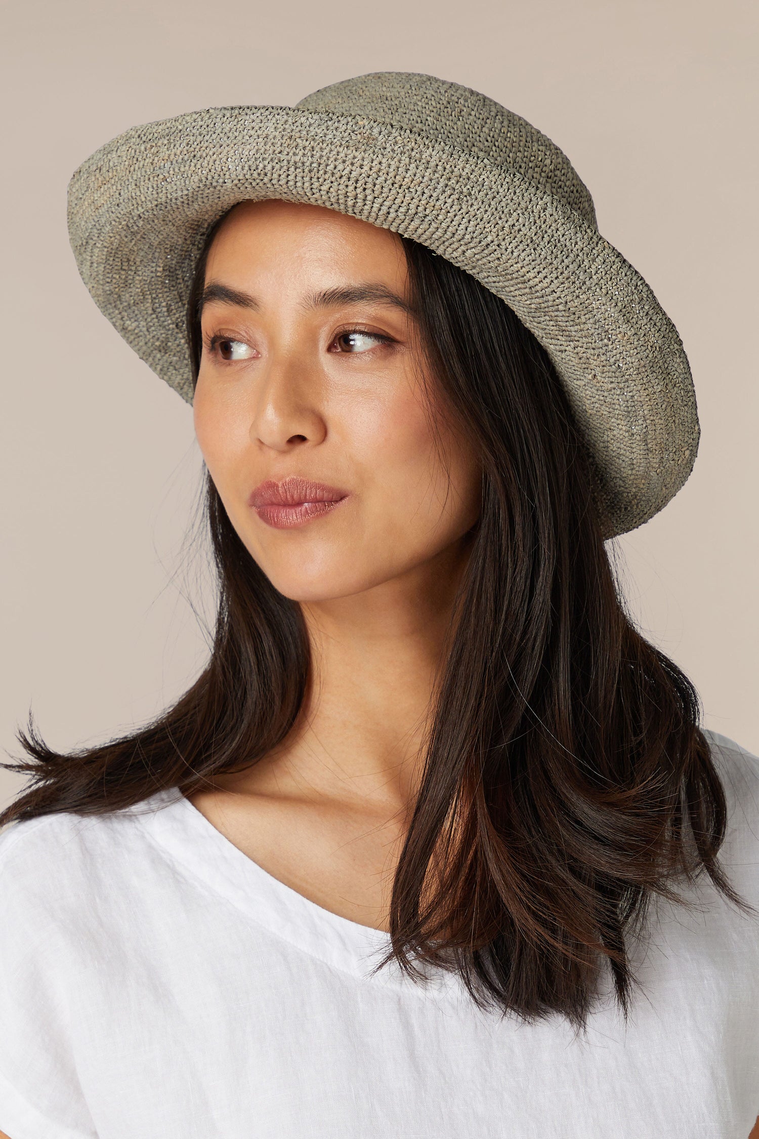 A woman wearing a Woven Raffia Hat and white top, gazing to the side.