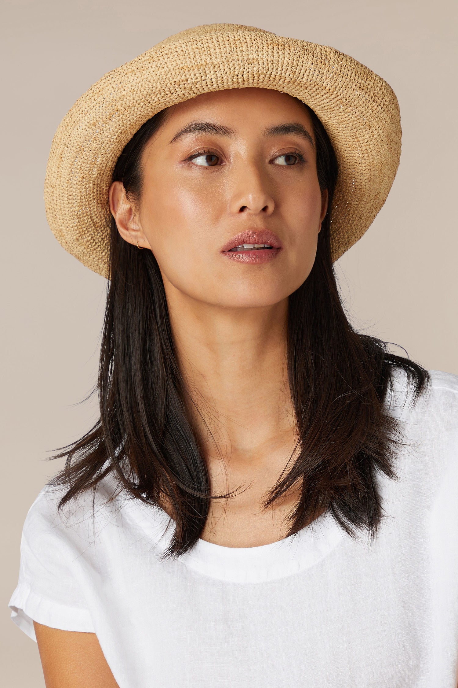 Woman in a Woven Raffia Hat and white top looking to the side.