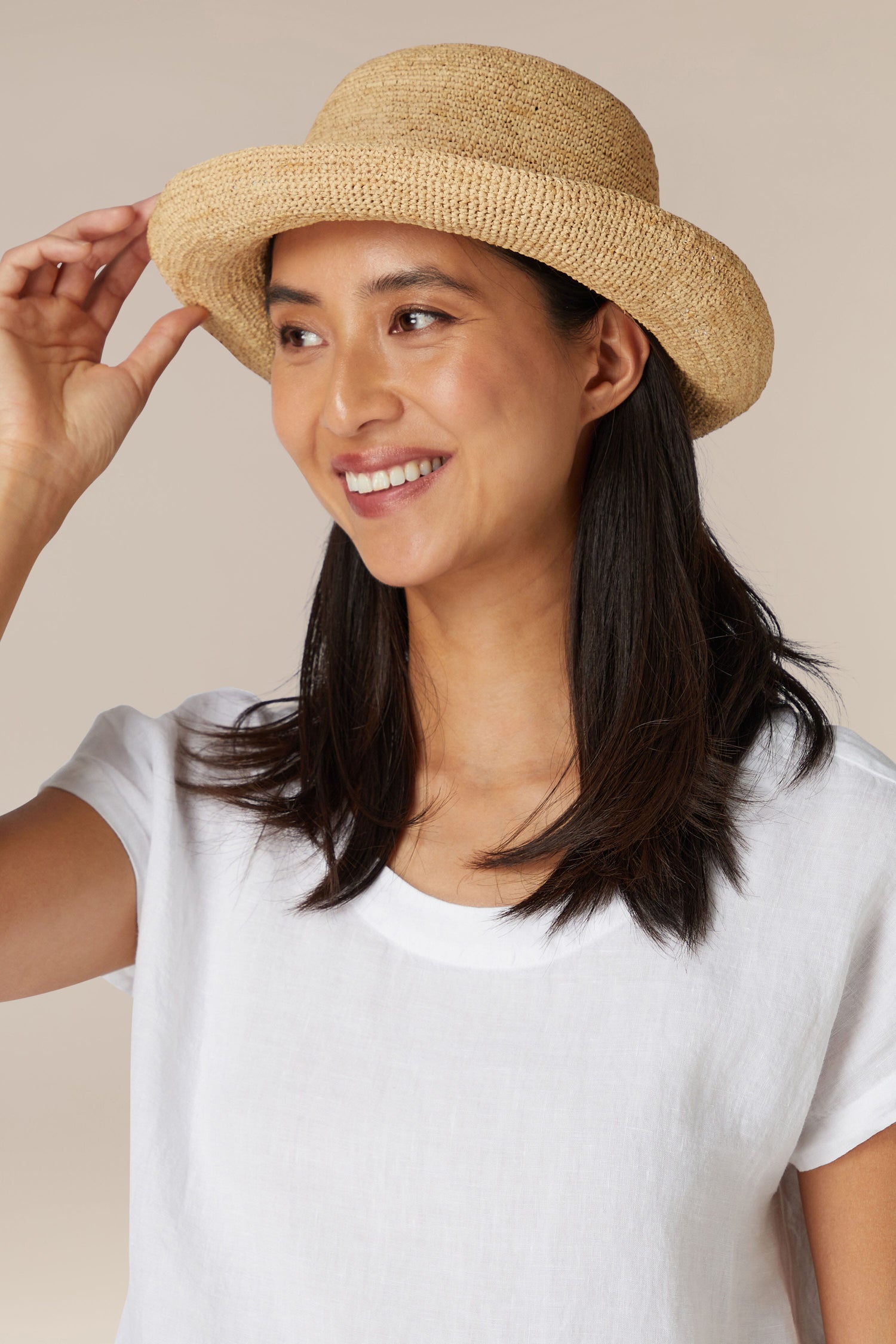 A smiling woman tilting a Woven Raffia Hat on her head.