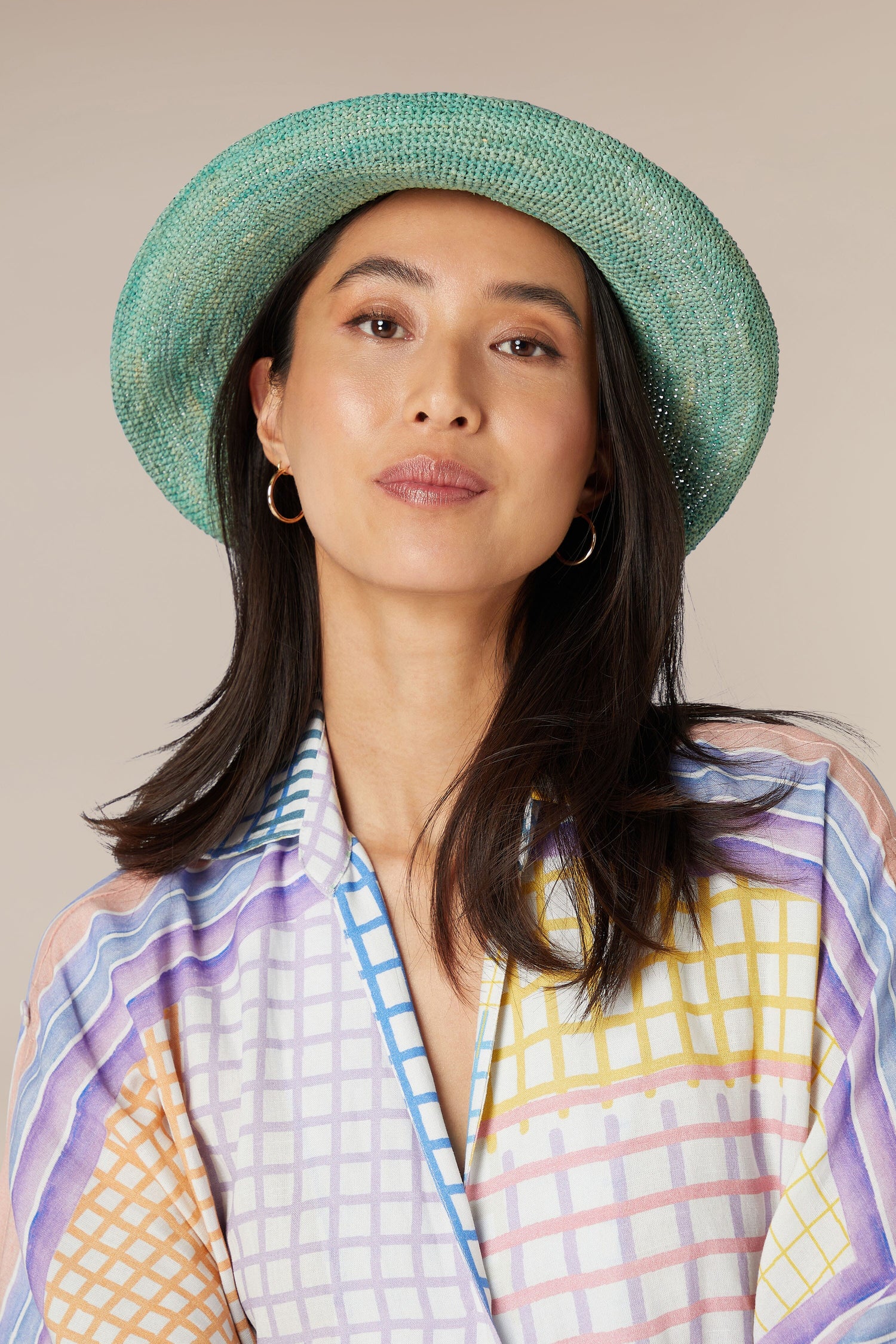 A woman wearing a Woven Raffia hat and a patterned blouse with hoop earrings.