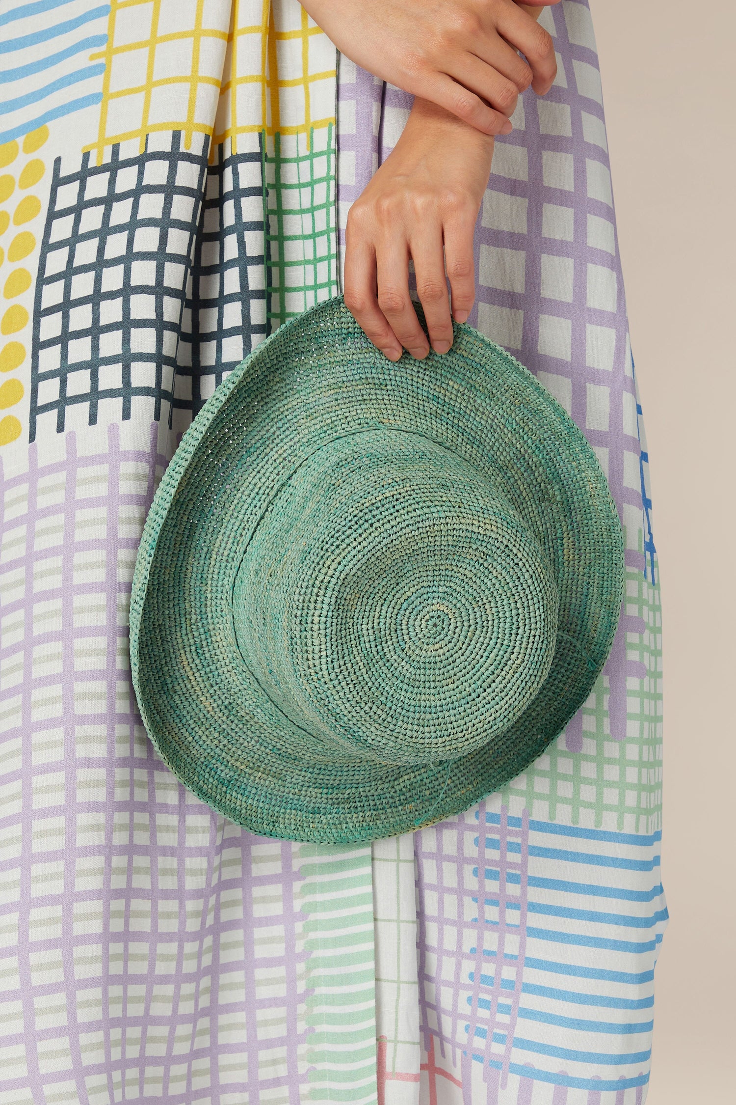 Person holding a Woven Raffia Hat against a colorful patterned dress.