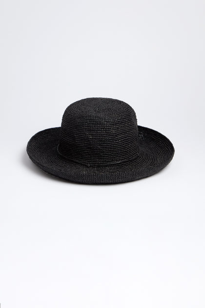 The Rabarany Handwoven Raffia Hat is a black straw hat with a wide brim and rounded crown, expertly crafted using Madagascar weaving techniques. Displayed on a plain white background, it highlights its lightweight and breathable design.