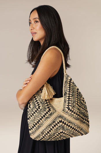 Woman posing with a hand-crafted black and beige Woven Bohemian Raffia tote bag.