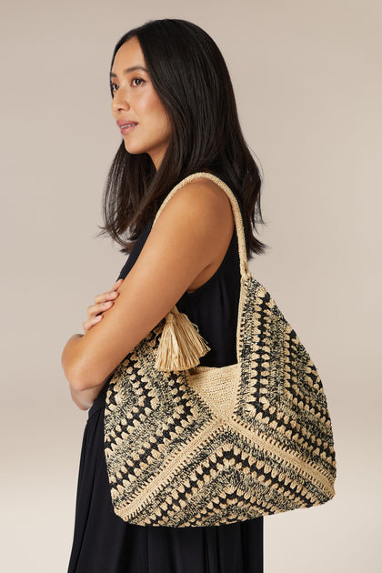 Woman posing with a hand-crafted black and beige Woven Bohemian Raffia tote bag.