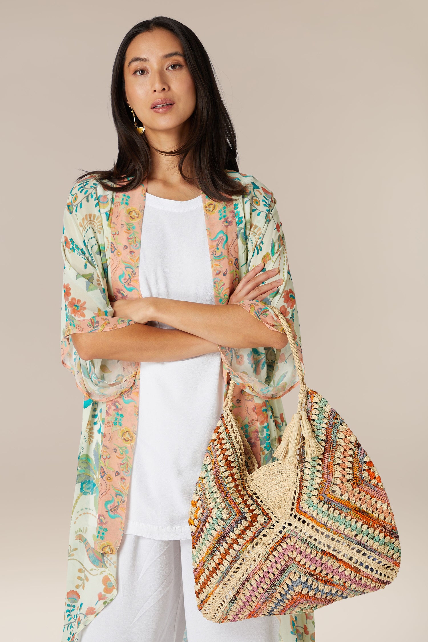 Woman in a white outfit and a floral kimono carrying a Woven Bohemian Raffia Bag.