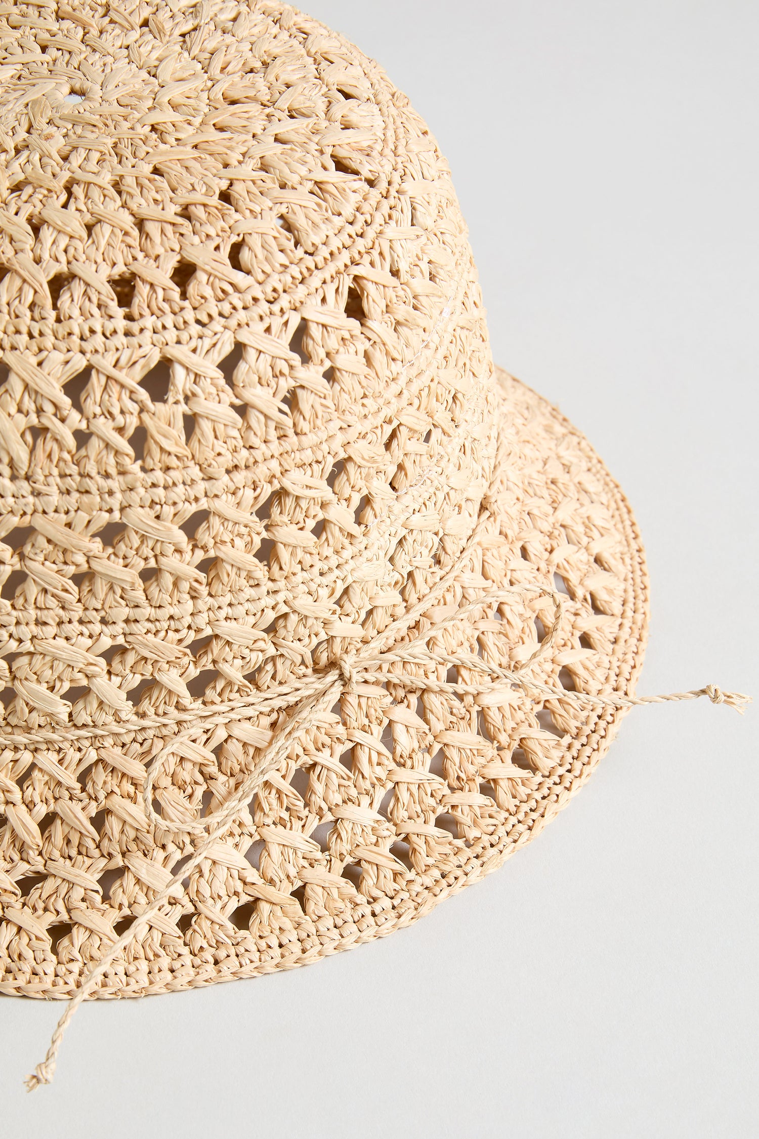 Close-up of the Handwoven Raffia Bucket Hat in beige from Madagascar, featuring a decorative braided band, displayed on a plain light background.