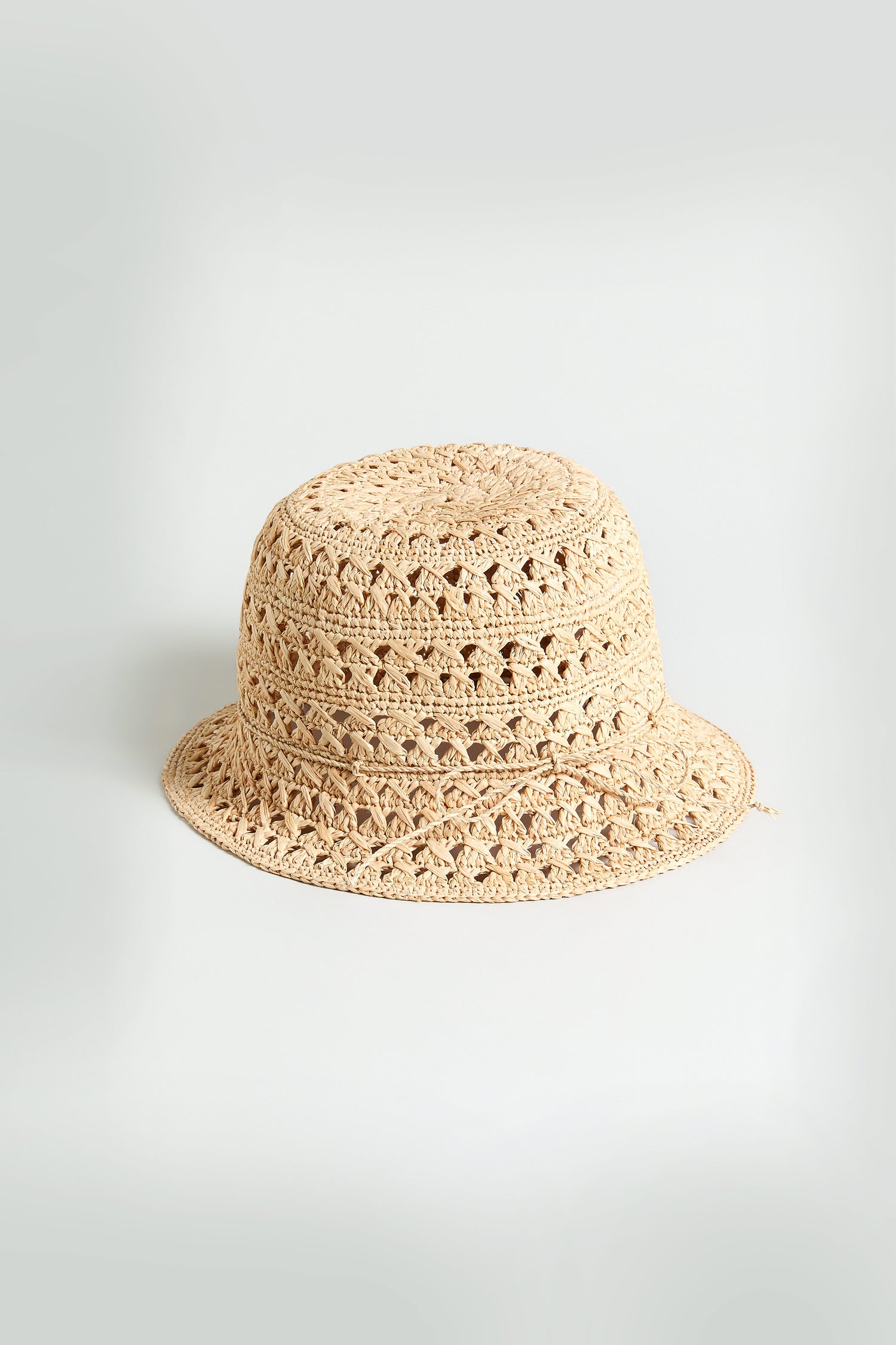 The Handwoven Raffia Bucket Hat, crafted in a beige crochet style from Madagascar straw, is displayed on a plain light background.