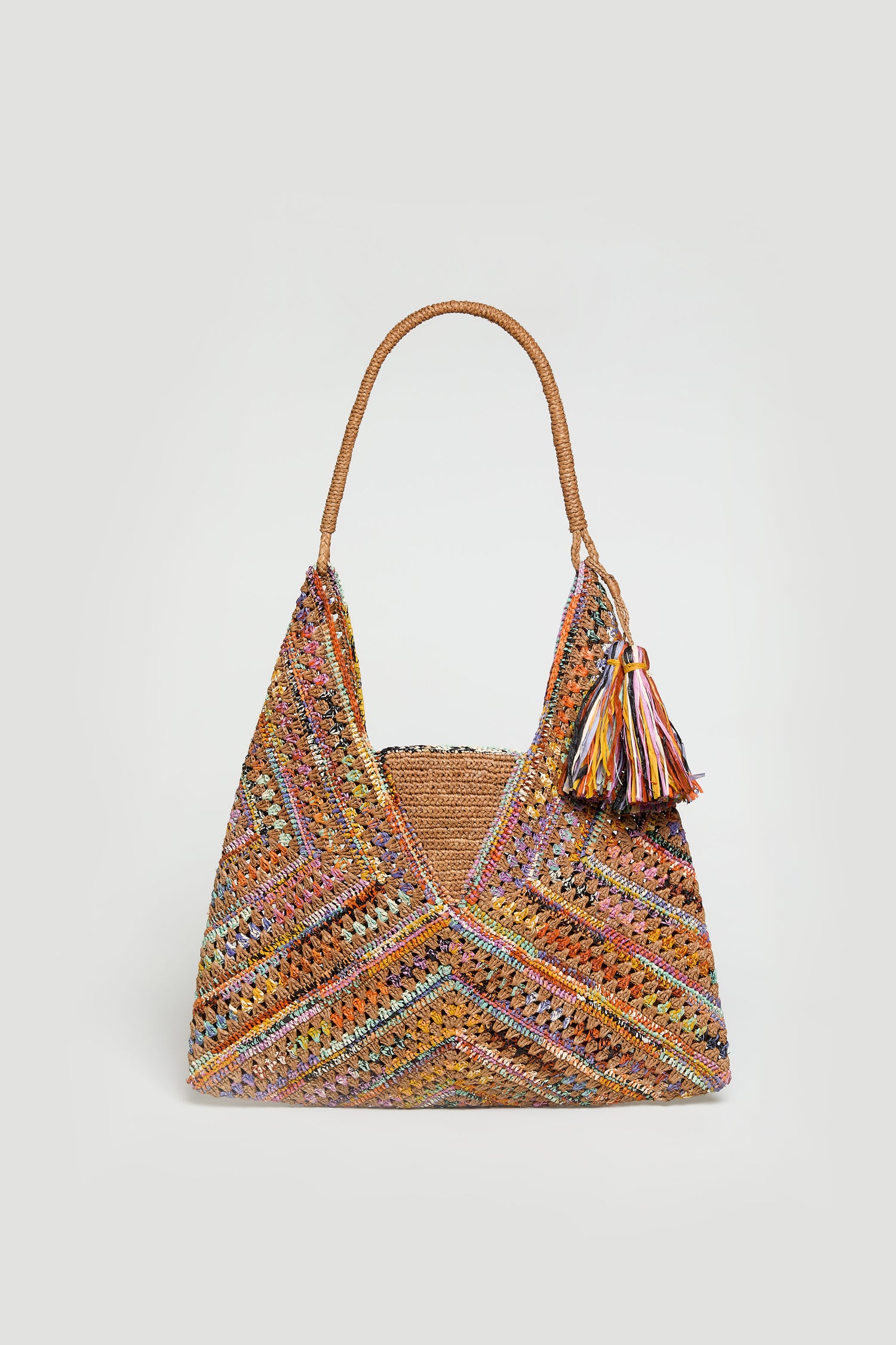 The Handwoven Raffia Harlequin Bag from Madagascar features a multicolored harlequin pattern, braided handles, and a tassel, showcased against a plain light background.