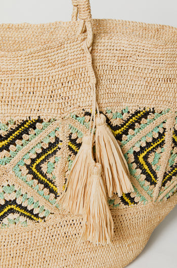 Close-up of the Handwoven Raffia Mosaic Bag, showcasing geometric patterns in black, yellow, and green, and two braided tassels on the handle.