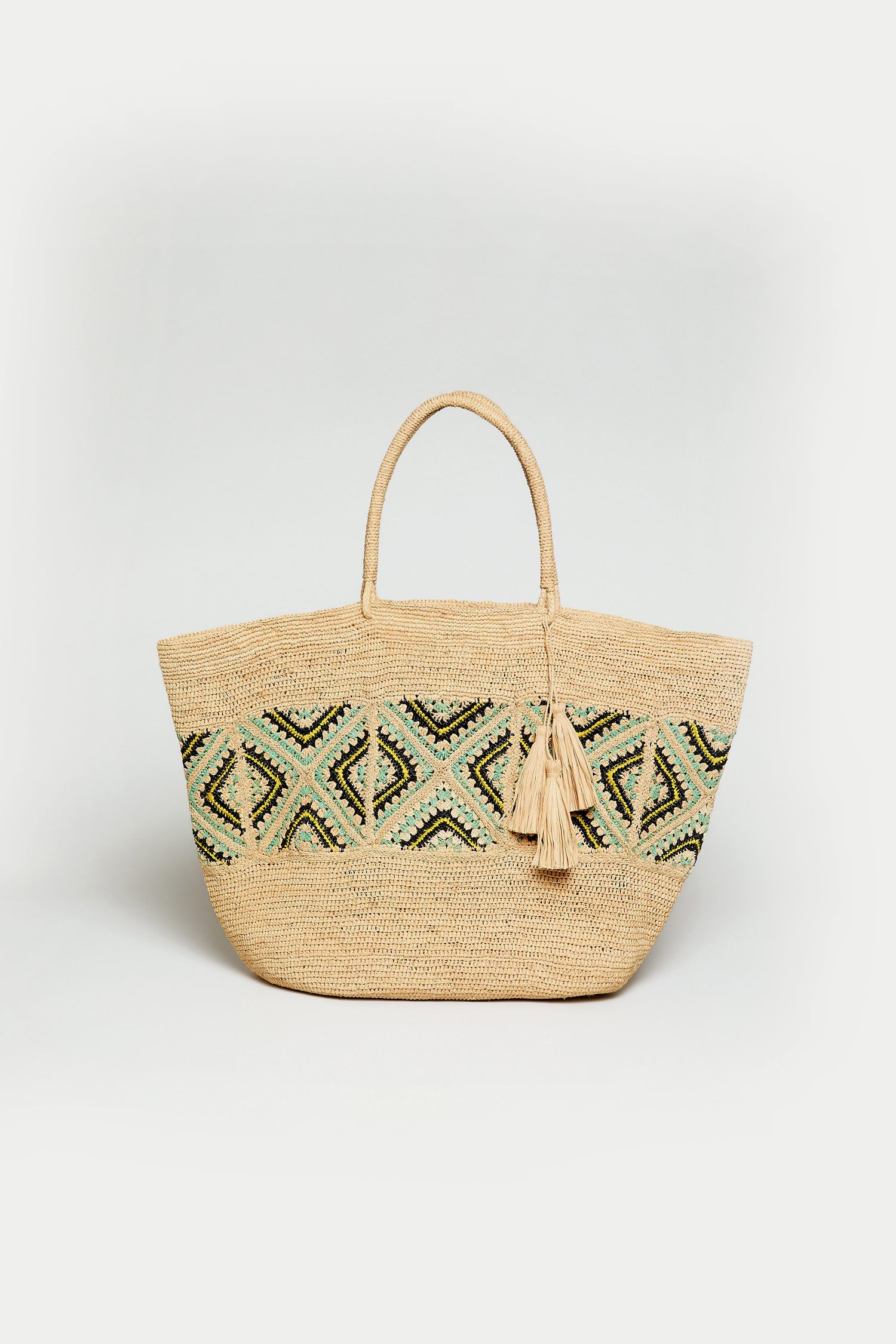 The Handwoven Raffia Mosaic Bag features two handles, a blue, green, and black geometric pattern, and two tassels attached to one handle.