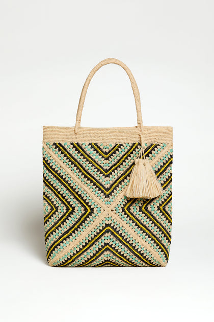 The Handwoven Raffia Mosaic Bag features a geometric zigzag pattern in beige, black, and green, two handles, and a tassel accent—a beautifully crafted artisan bag from Madagascar.