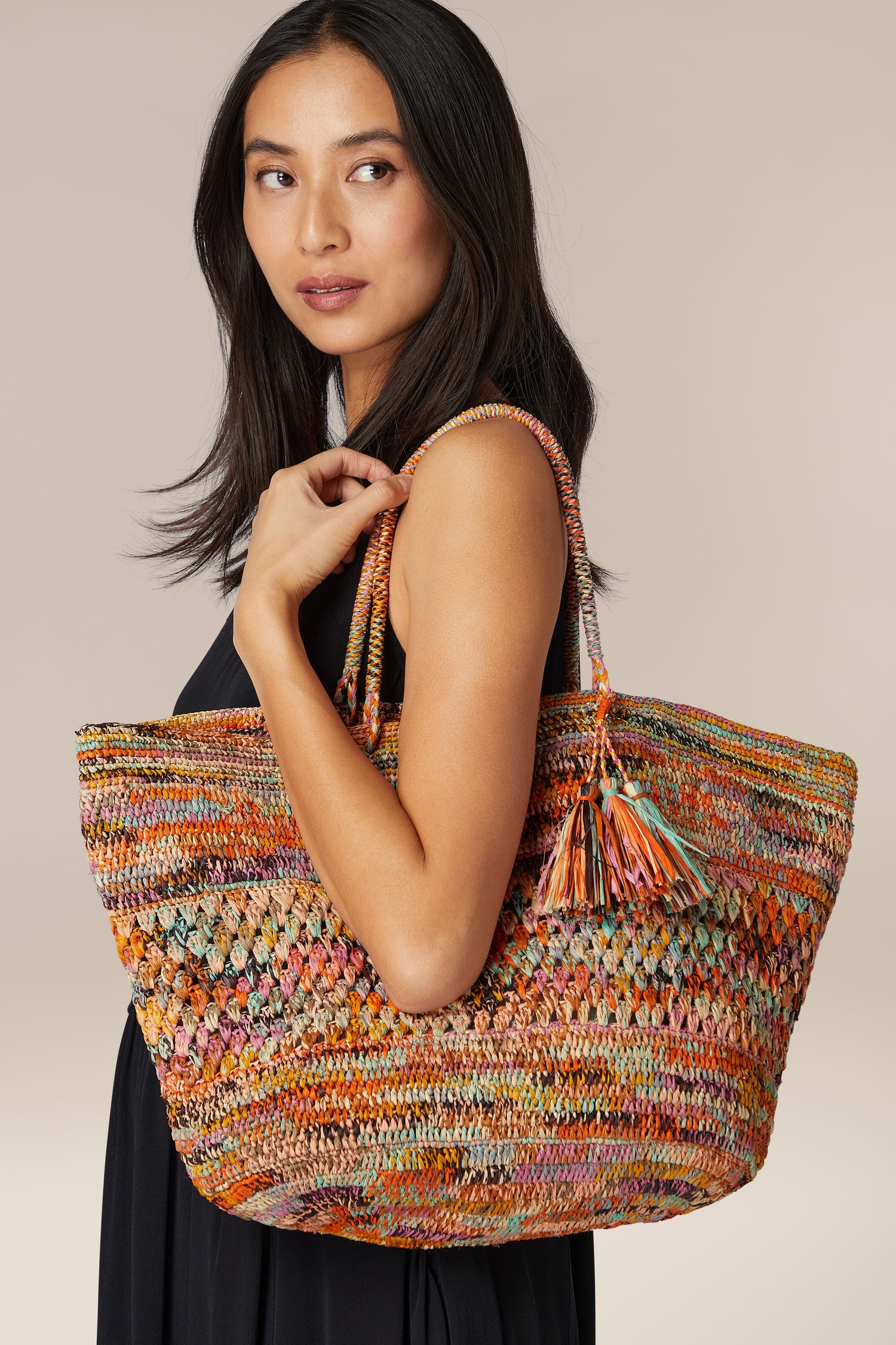 Woman holding a Woven Rainbow Raffia Bag, crafted by Madagascar artisans, over her shoulder.