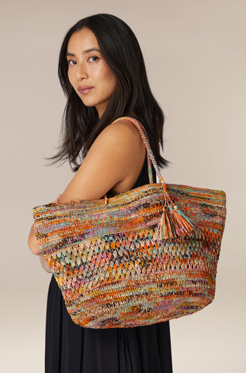 Young woman posing with a Woven Rainbow Raffia Bag over her shoulder, created by Madagascar artisans.