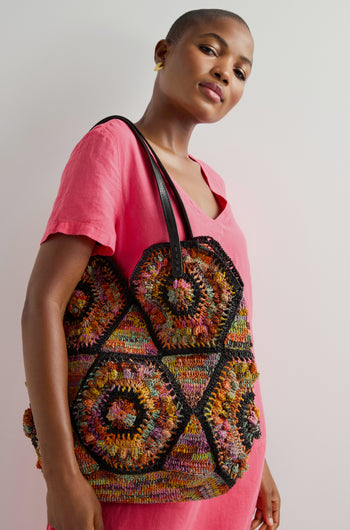 A person in a pink dress carries a Handwoven Aztec Raffia Bag featuring geometric patterns, highlighting exquisite artisanal craftsmanship.