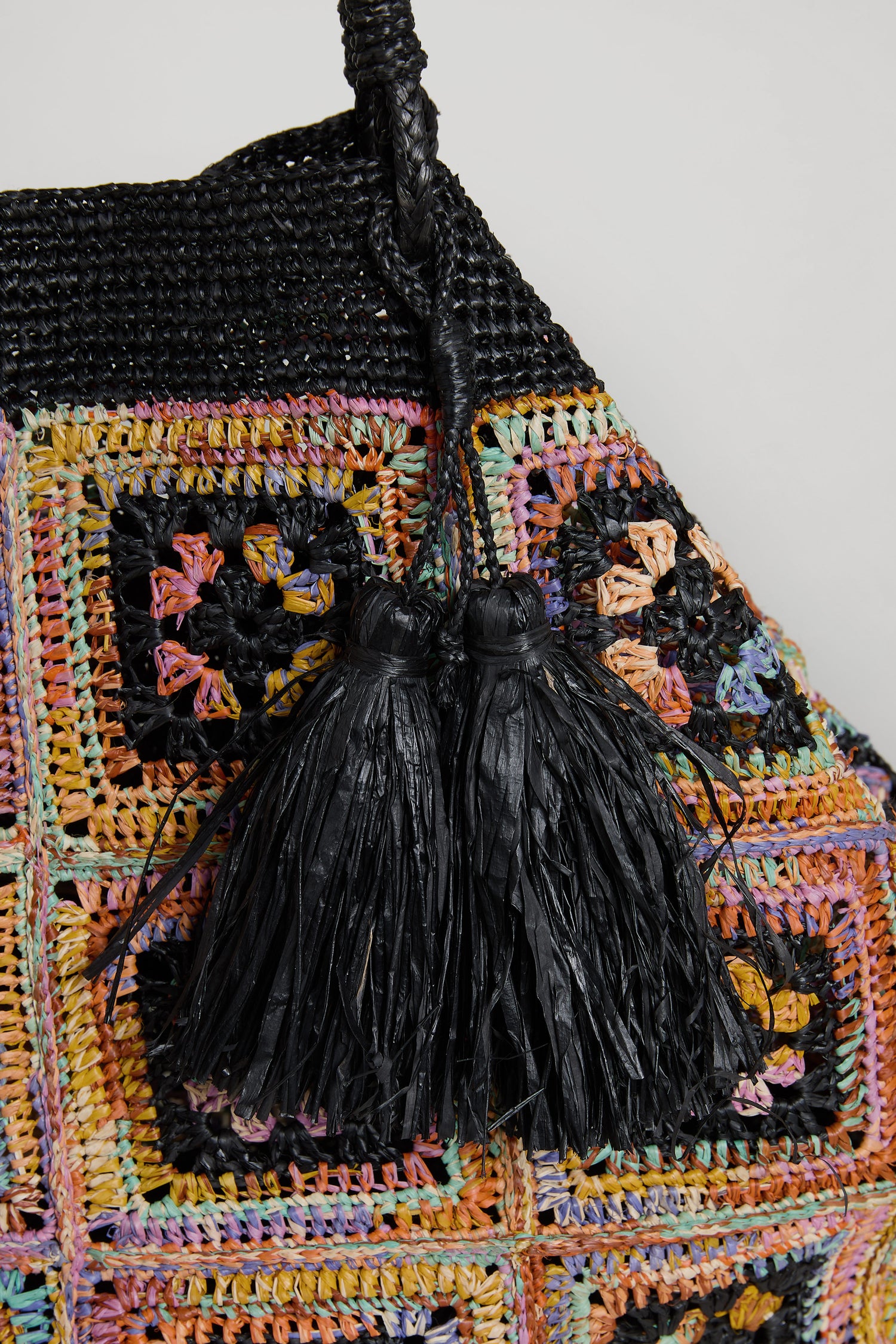 Close-up of the Handwoven Raffia Crochet Bag from Madagascar, showcasing a colorful patchwork crochet design and two black raffia tassels by the handle.