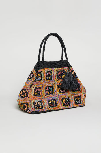 The Handwoven Raffia Crochet Bag from Madagascar features a vibrant multicolored design with black handles, a black tassel, and striking square motifs.