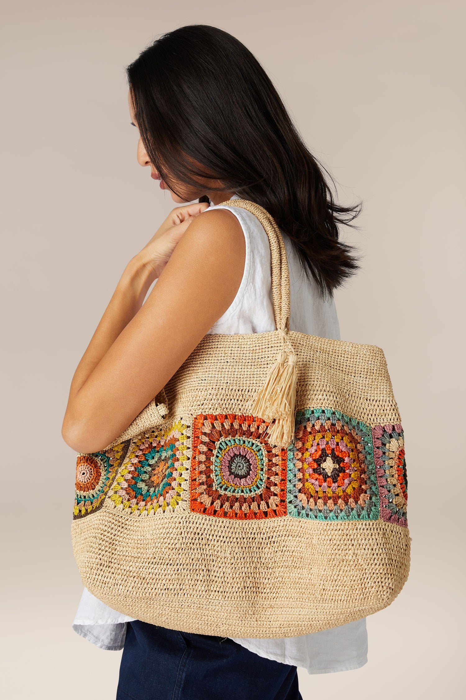 Woman carrying a large Aztec Woven Raffia Bag with colorful crochet detailing.