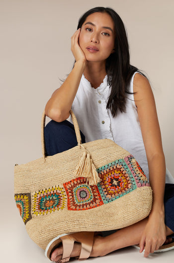 A woman sitting with a colorful Aztec woven Raffia Bag.