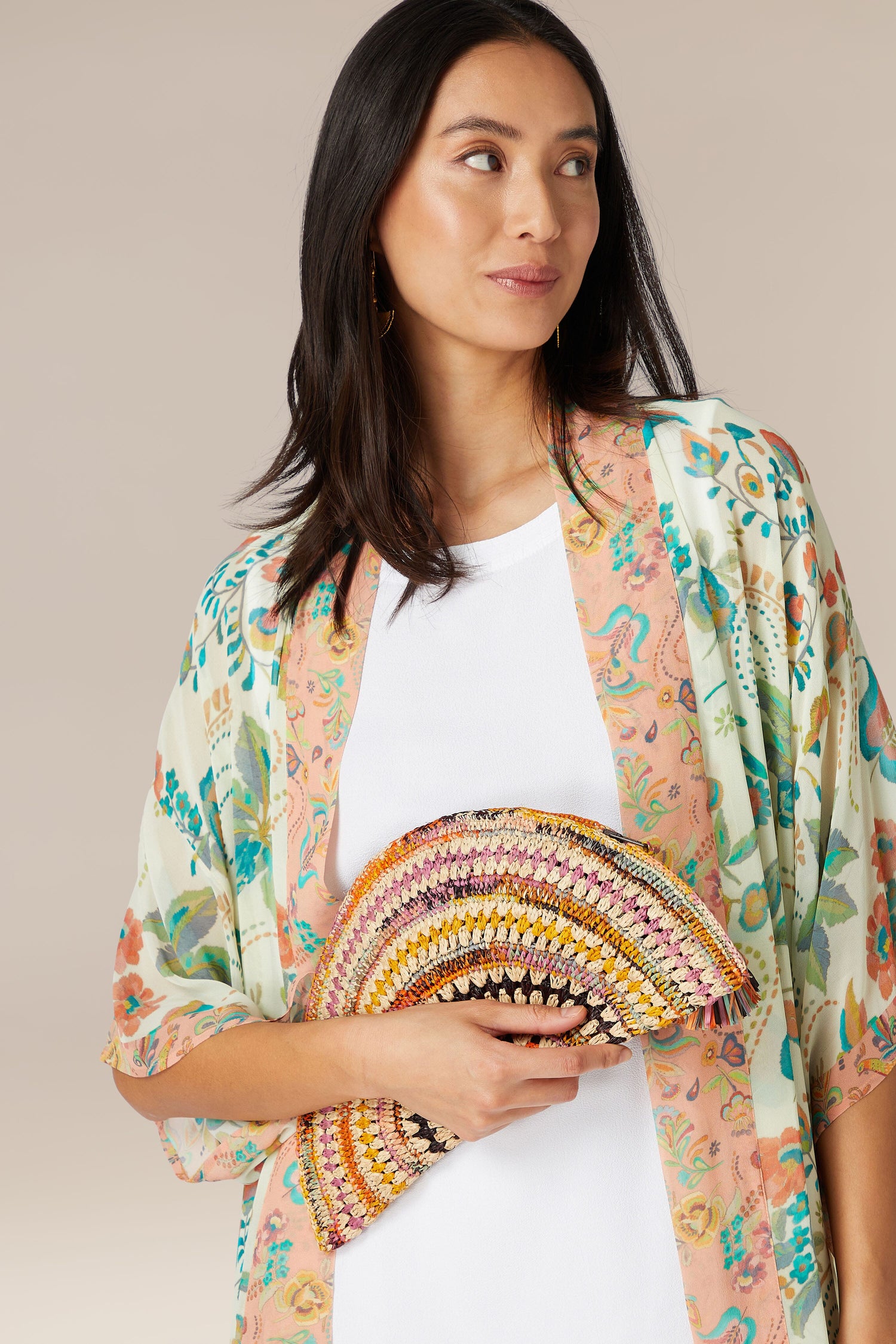 Woman holding a colorful, Woven Half Moon Raffia Clutch while wearing a floral print cardigan.