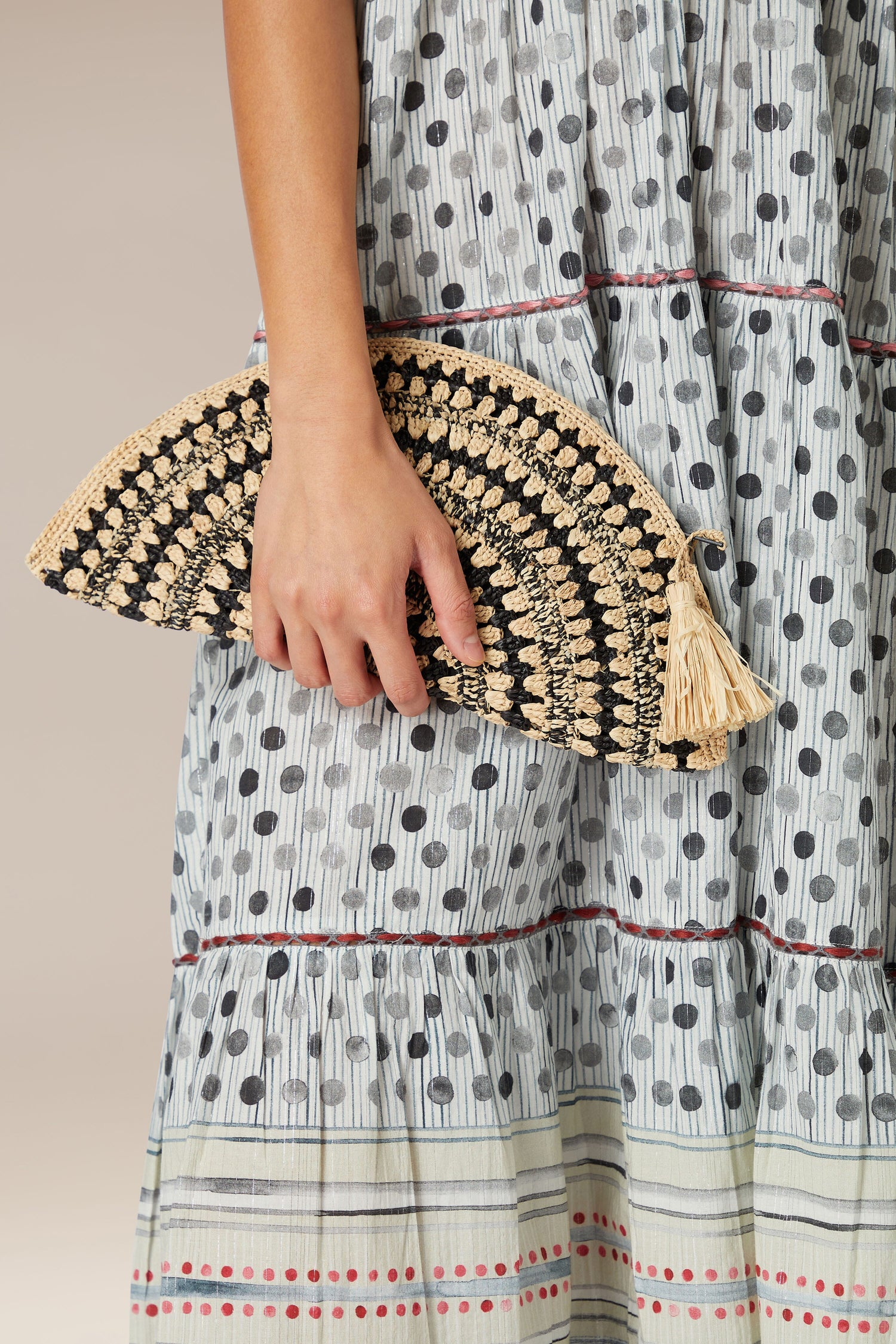 A person holding a Woven Half Moon Raffia Clutch against a printed dress.