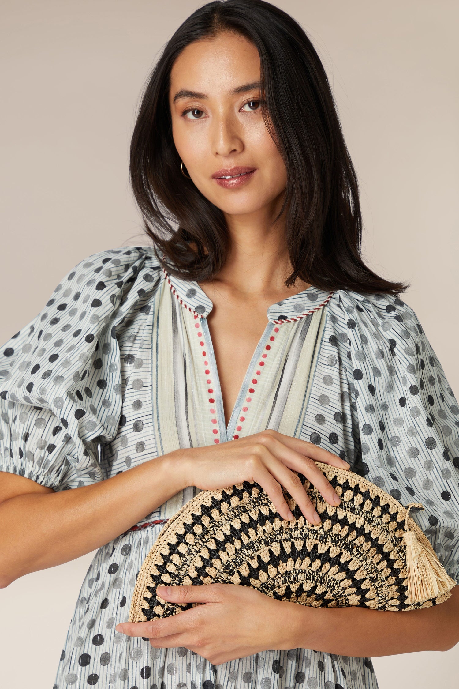 Woman holding a Woven Half Moon Raffia Clutch while wearing a patterned blouse.