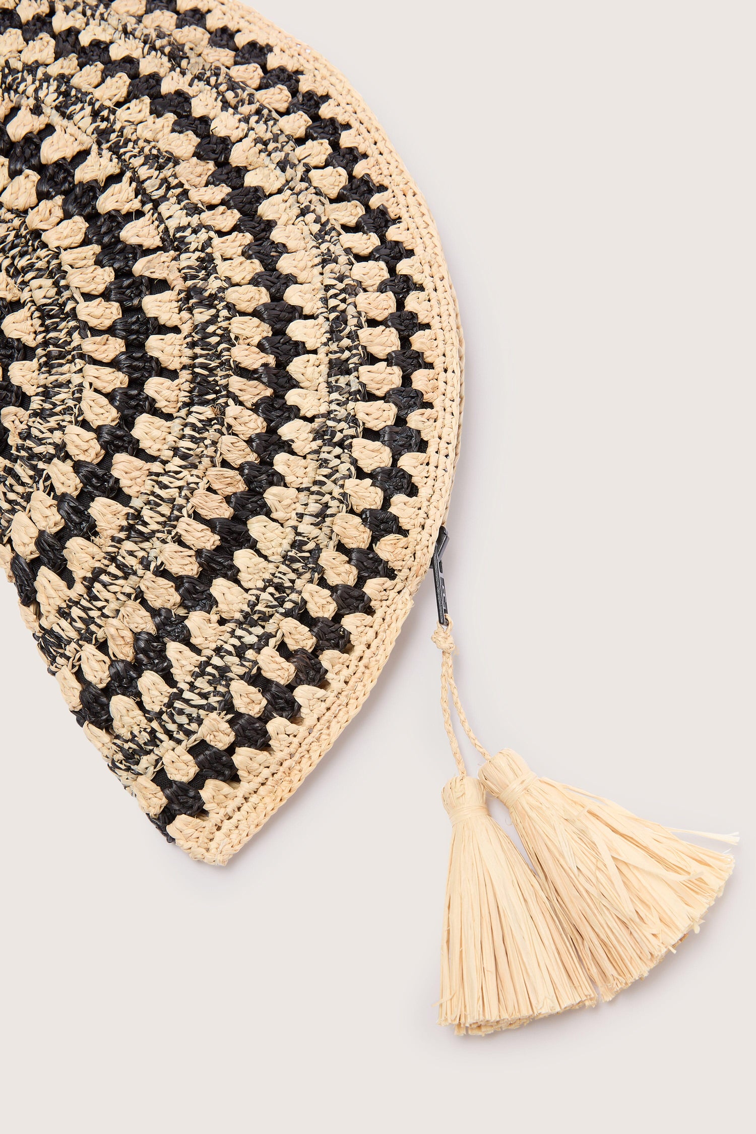 Round woven Half Moon raffia clutch with a black, beige, and cream pattern and a tassel detail, featuring Madagascar hand-crafted natural fibers.