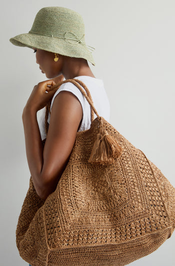 A person in a green hat and white shirt holds a large Handwoven Crochet Basket with a tassel, highlighting sustainable craftsmanship against a plain background.