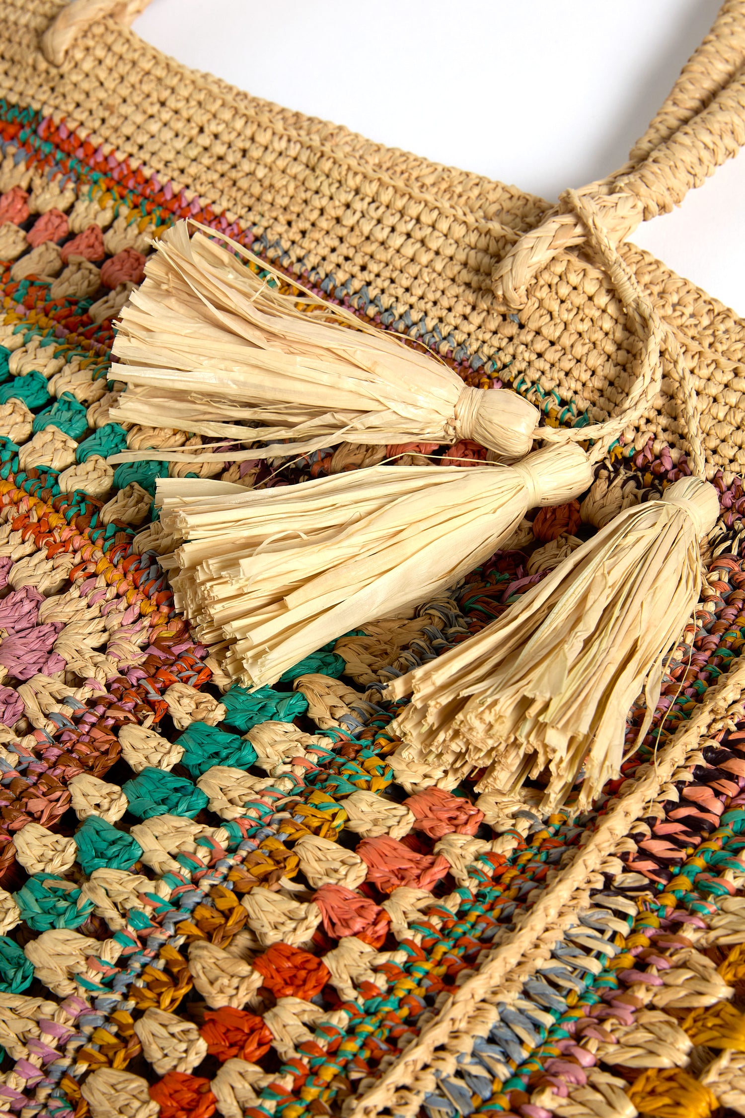 Close-up of the Handwoven Crochet Raffia Bag, featuring a detailed straw crochet design with vibrant patterns and two large raffia tassels near the handle.