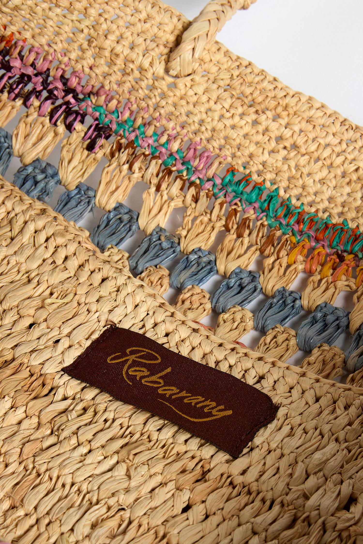 Close-up of the Handwoven Crochet Raffia Bag, featuring vibrant woven details and a brown fabric label with gold script reading "Relaxury.