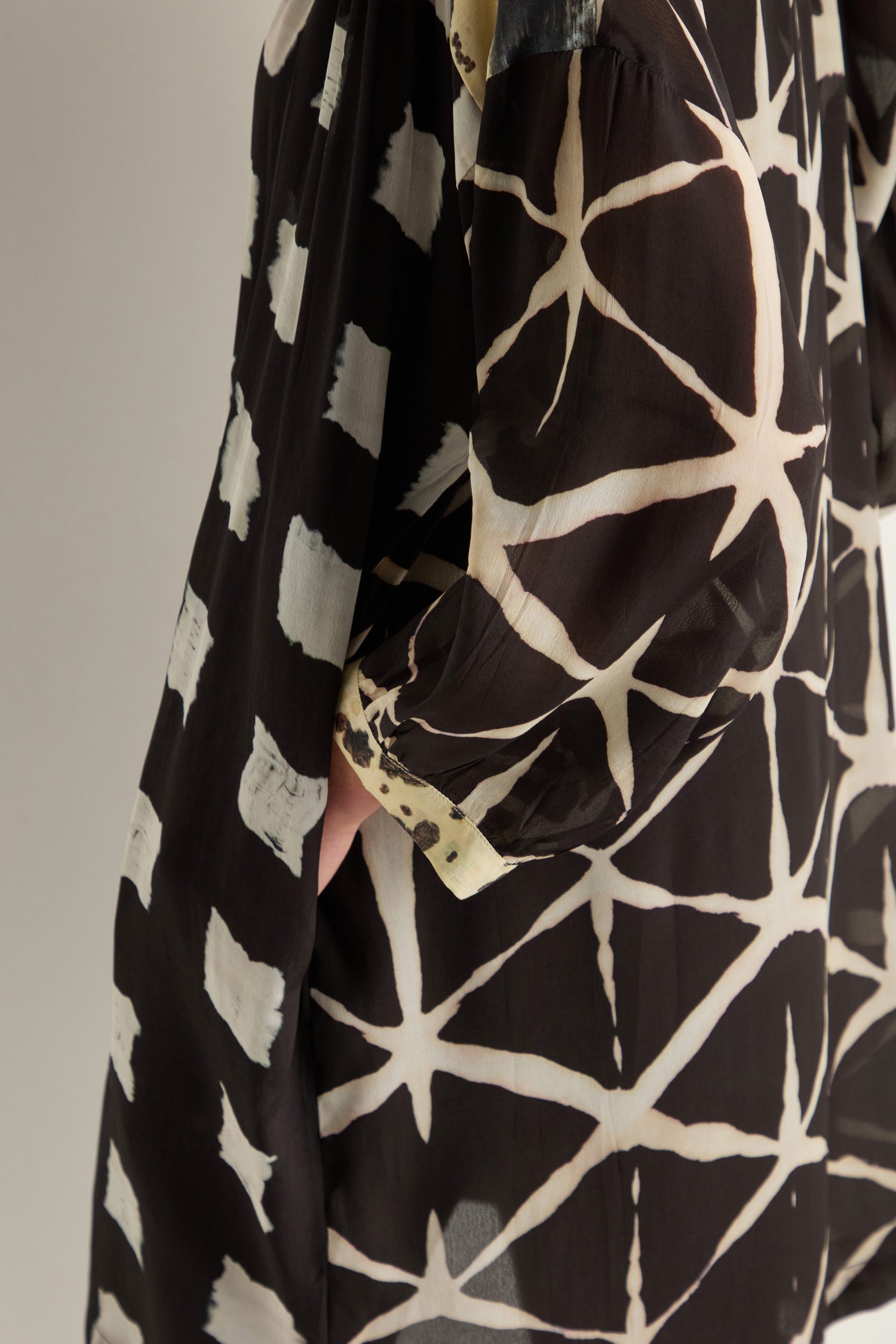 Close-up of a person wearing the Shibori Print Long Shirt, a relaxed fit garment featuring black and white geometric star and square patterns.