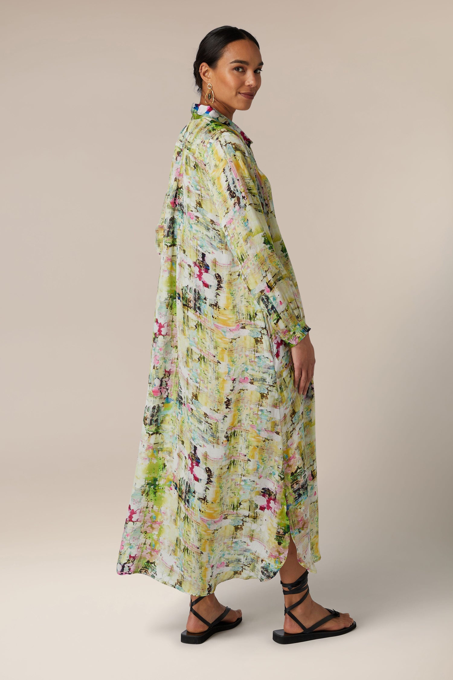 The back view of a woman wearing a maxi length, floral printed Pelia Button Front Dress.