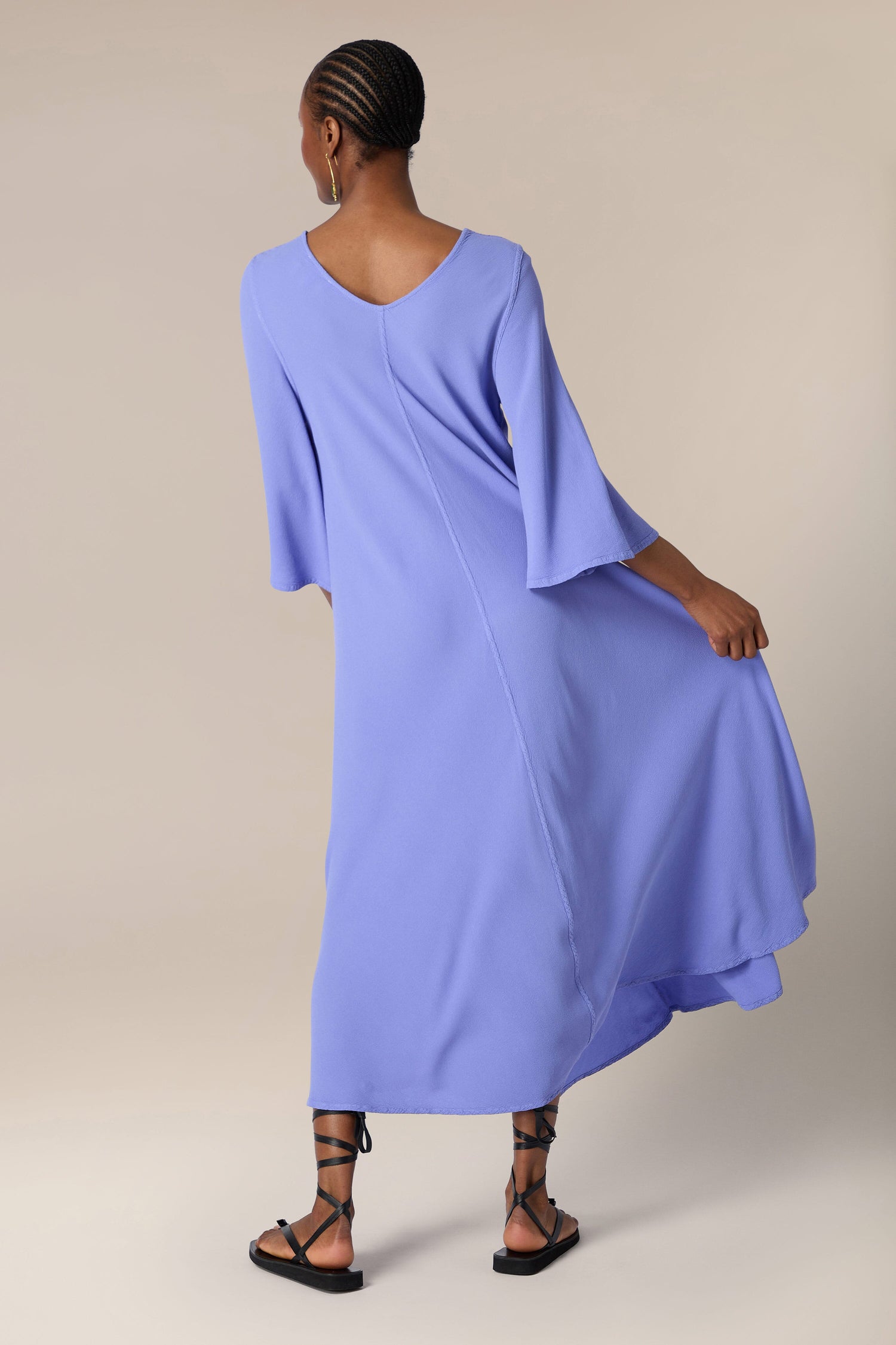 A woman in a stylish, flowing blue Crepe Maxi Dress and black sandals viewed from behind.