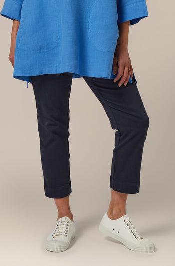 A person standing in blue tunic and navy Stretch Cotton Slim Crop Trouser with white sneakers.