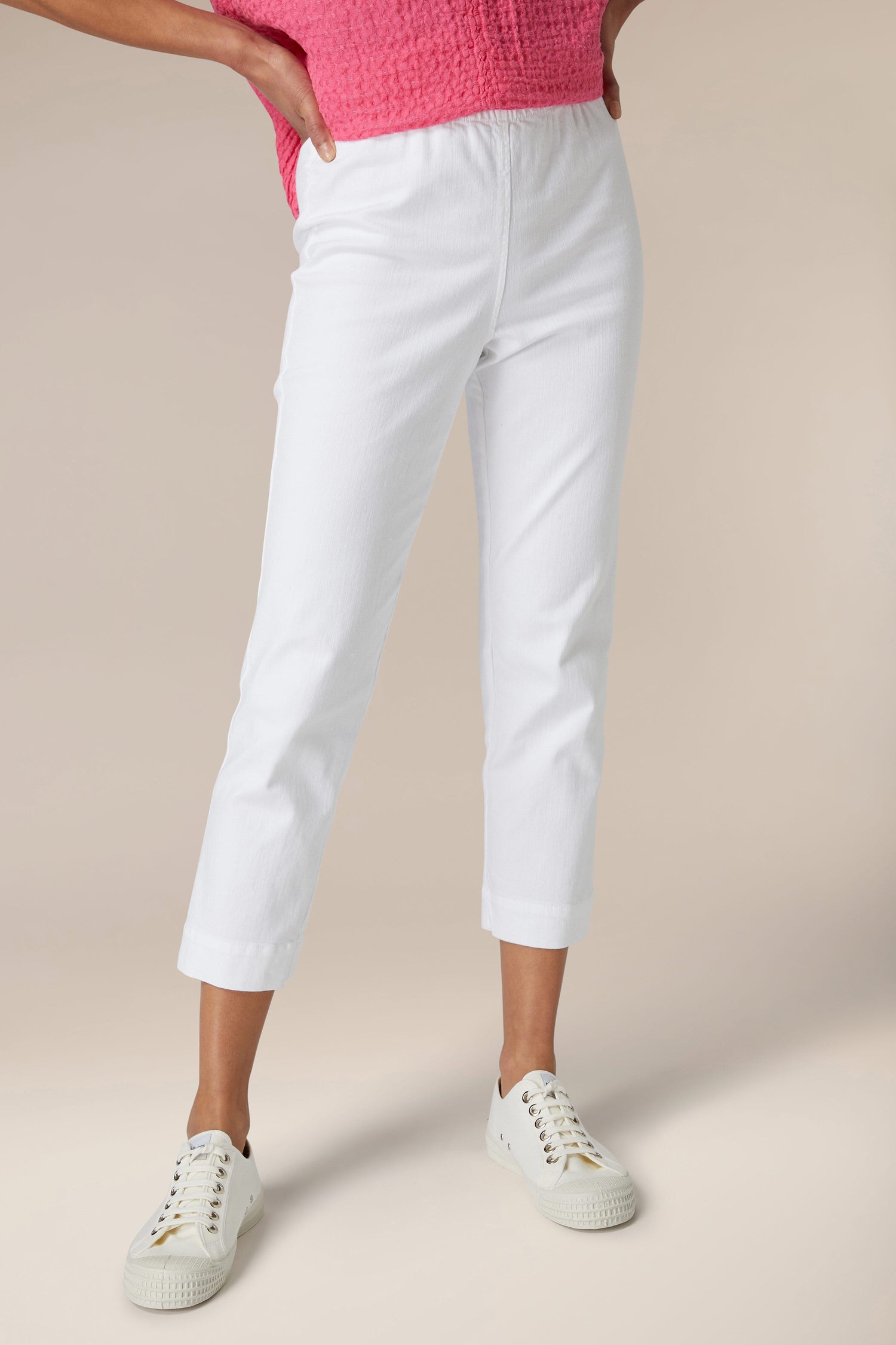 A person standing in white Stretch Cotton Slim Trousers and white sneakers paired with a pink top.