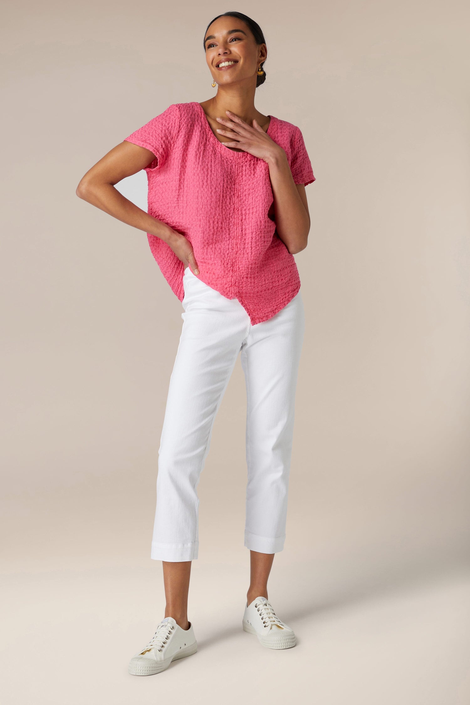 A woman posing in a pink top, white Stretch Cotton Slim Trousers, and white sneakers.