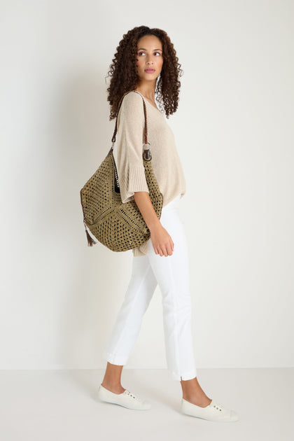 Woman with curly hair wears a beige top, Stretch Cotton White Slim Trousers, white shoes, and carries a large patterned shoulder bag while standing against a plain white background.
