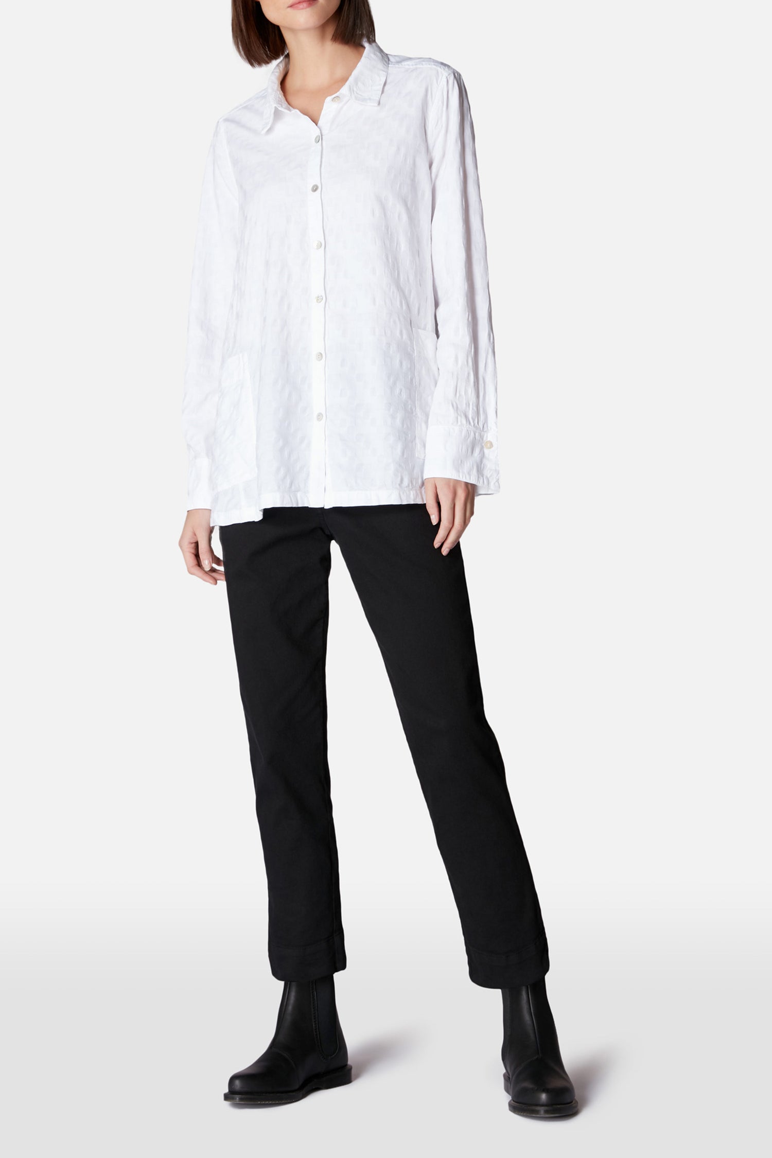 Person wearing a loose white button-up shirt, Black Stretch Cotton Slim Trouser, and black ankle boots, standing against a plain light background.