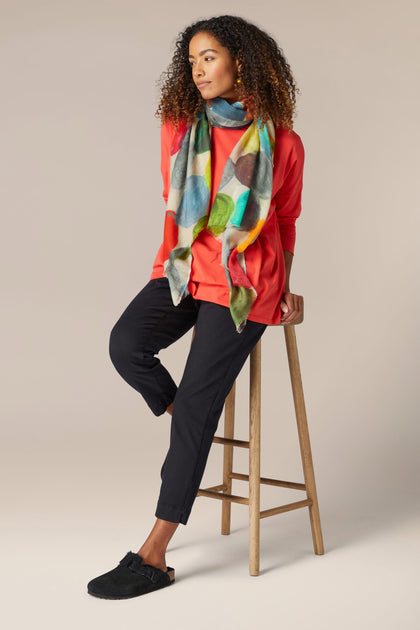 A woman is sitting on a stool wearing Stretch Cotton Slim Trousers, showcasing her timeless style.