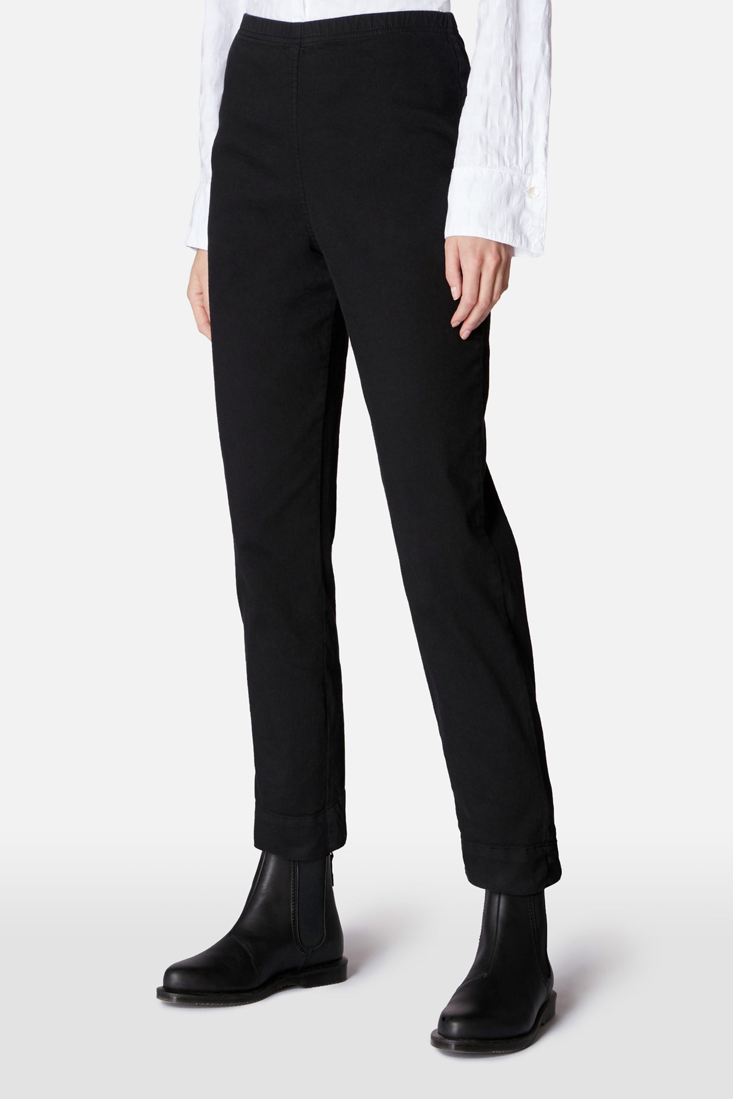 Person wearing Black Stretch Cotton Slim Trouser, a white textured long-sleeve shirt, and black ankle boots against a plain light background. Upper body partially out of frame.