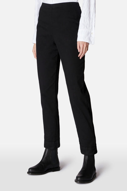Person wearing Black Stretch Cotton Slim Trouser, a white textured long-sleeve shirt, and black ankle boots against a plain light background. Upper body partially out of frame.
