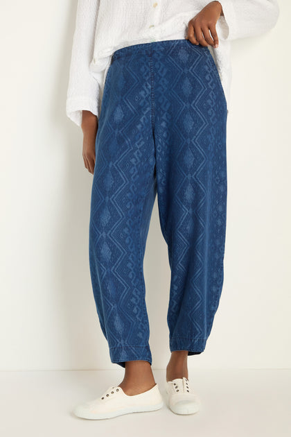 A person wears Light Denim Diamond Patchwork Print Bubble Trousers with an elasticated waistband, styled with a white textured button-up shirt and white sneakers, standing against a plain light-colored background.