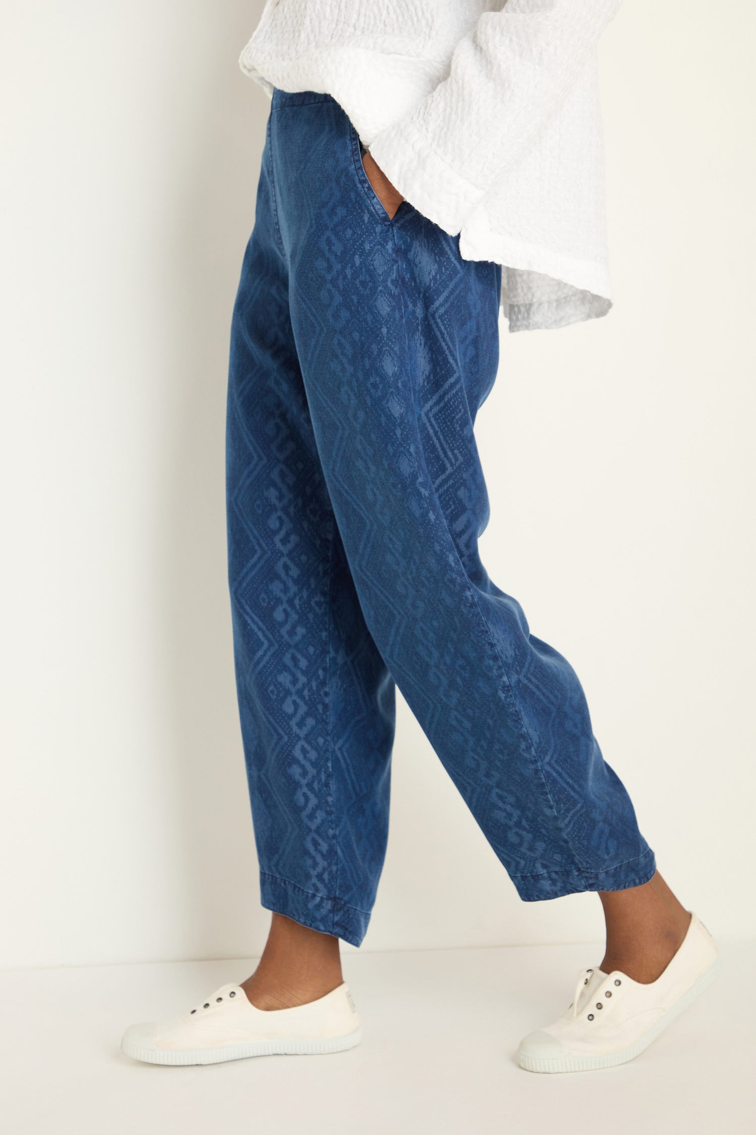 Person wearing Light Denim Diamond Patchwork Print Bubble Trousers with an elasticated waistband, a white textured long-sleeve top, and white slip-on shoes, standing against a plain background.