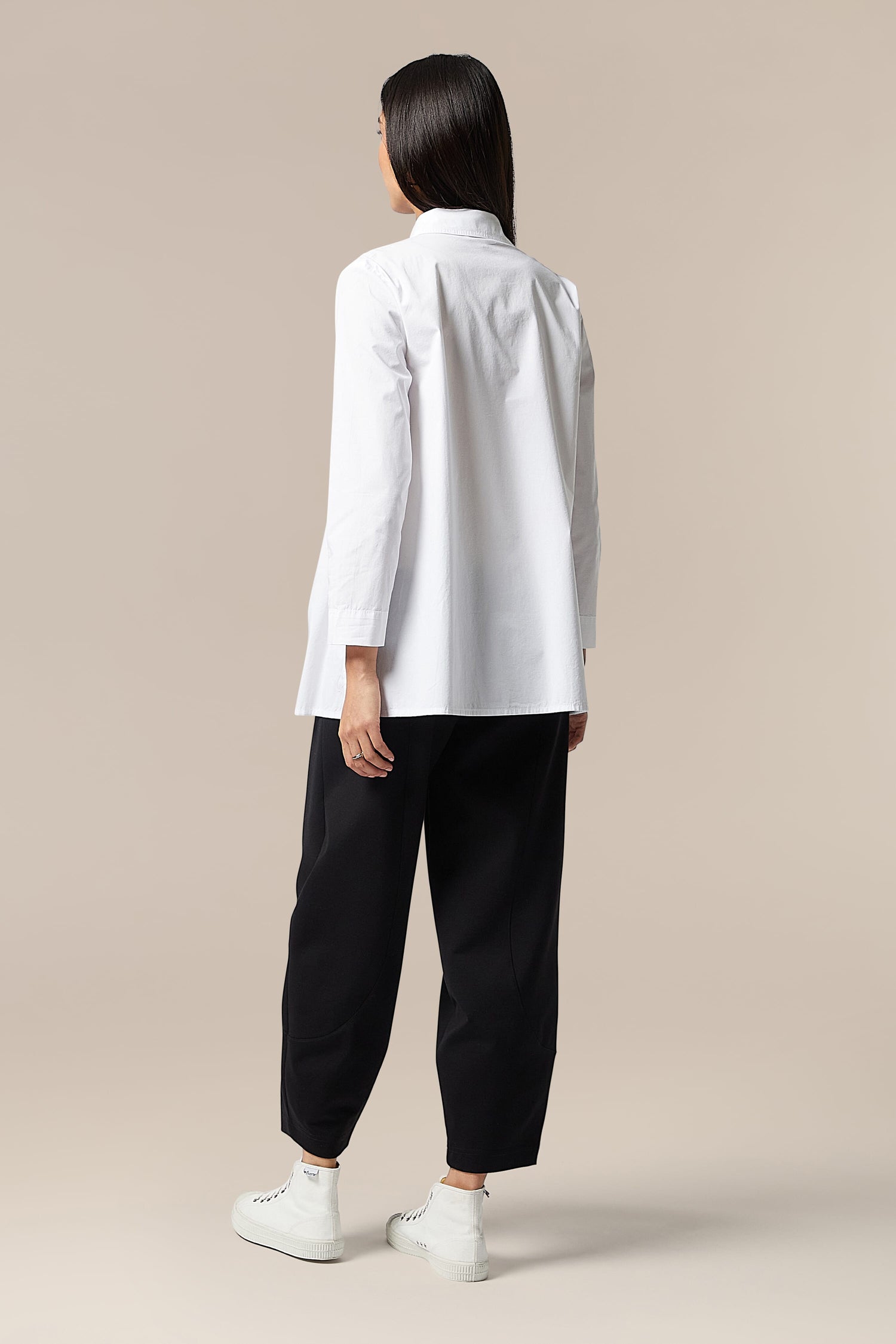 The elegant back view of a woman wearing a Paper Cotton Shirt and black pants.